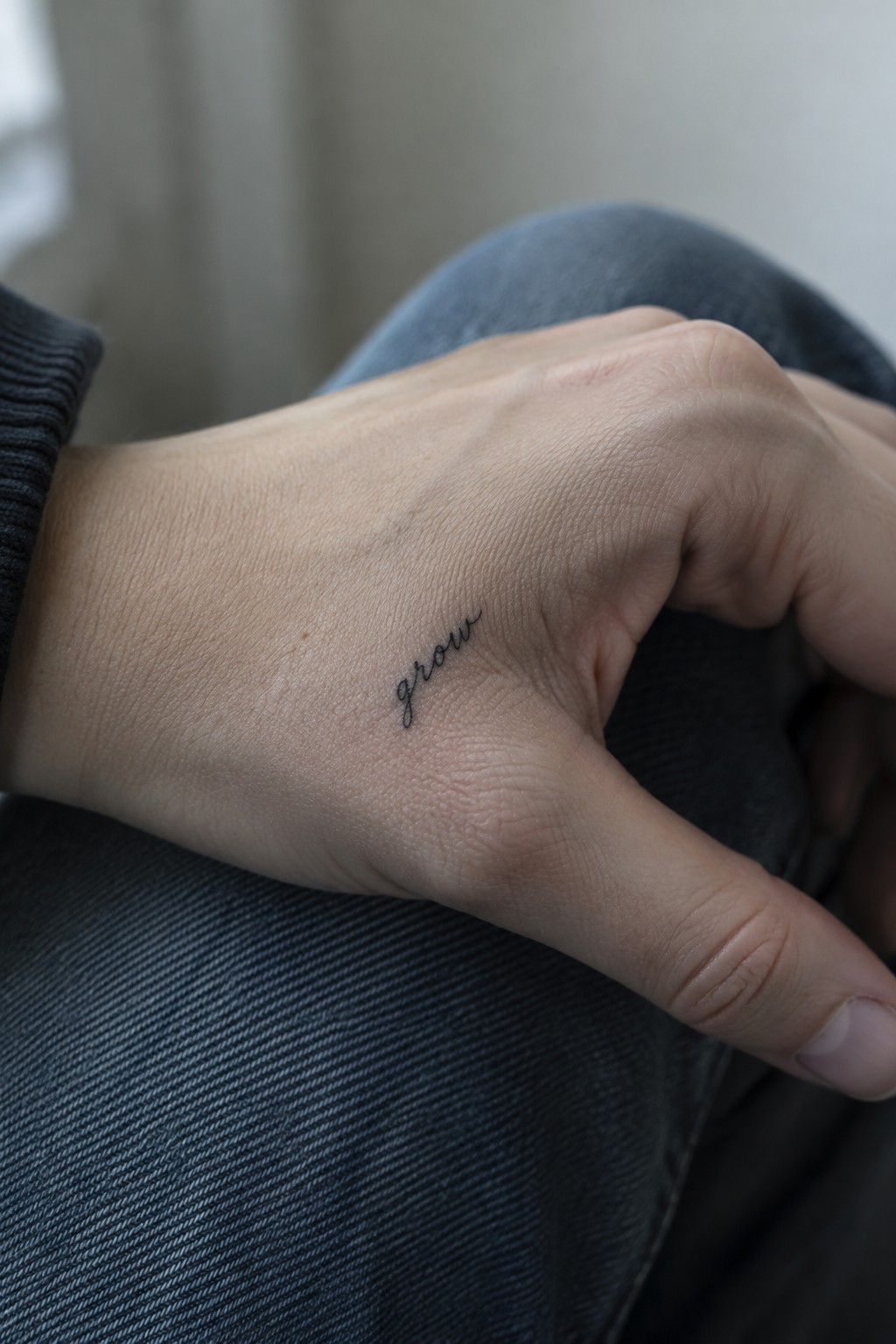 Close up of a small cursive tattoo spelling the word grow on the side of a hand.