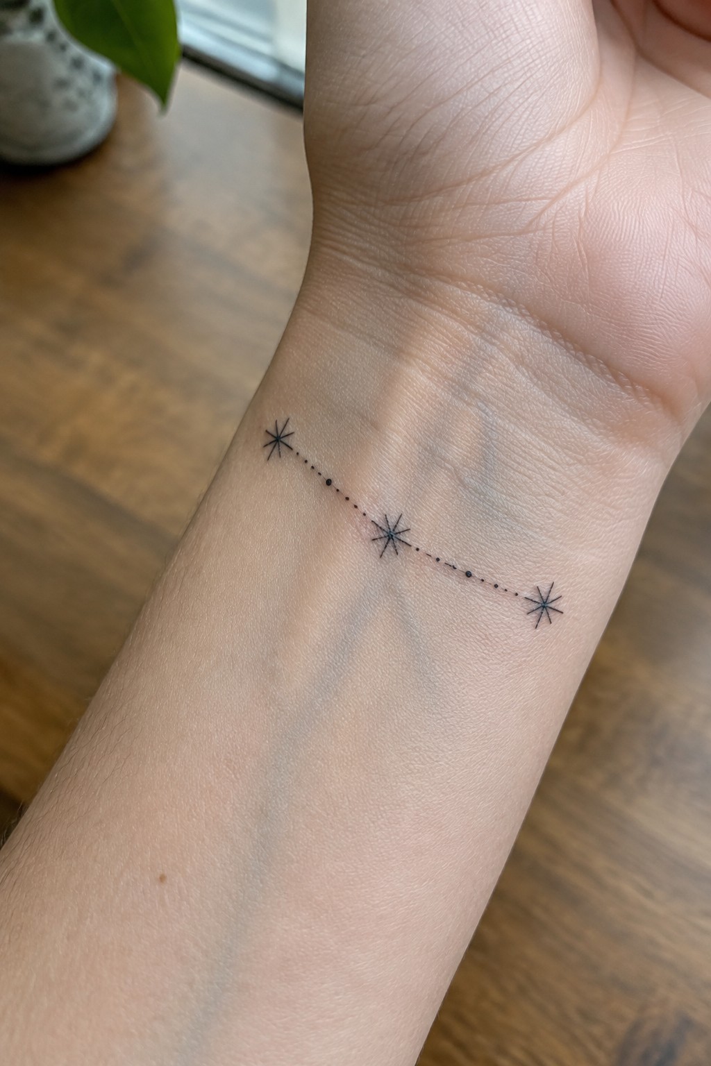 A minimalist wrist tattoo showing three small stars connected by a dotted line in fine black ink