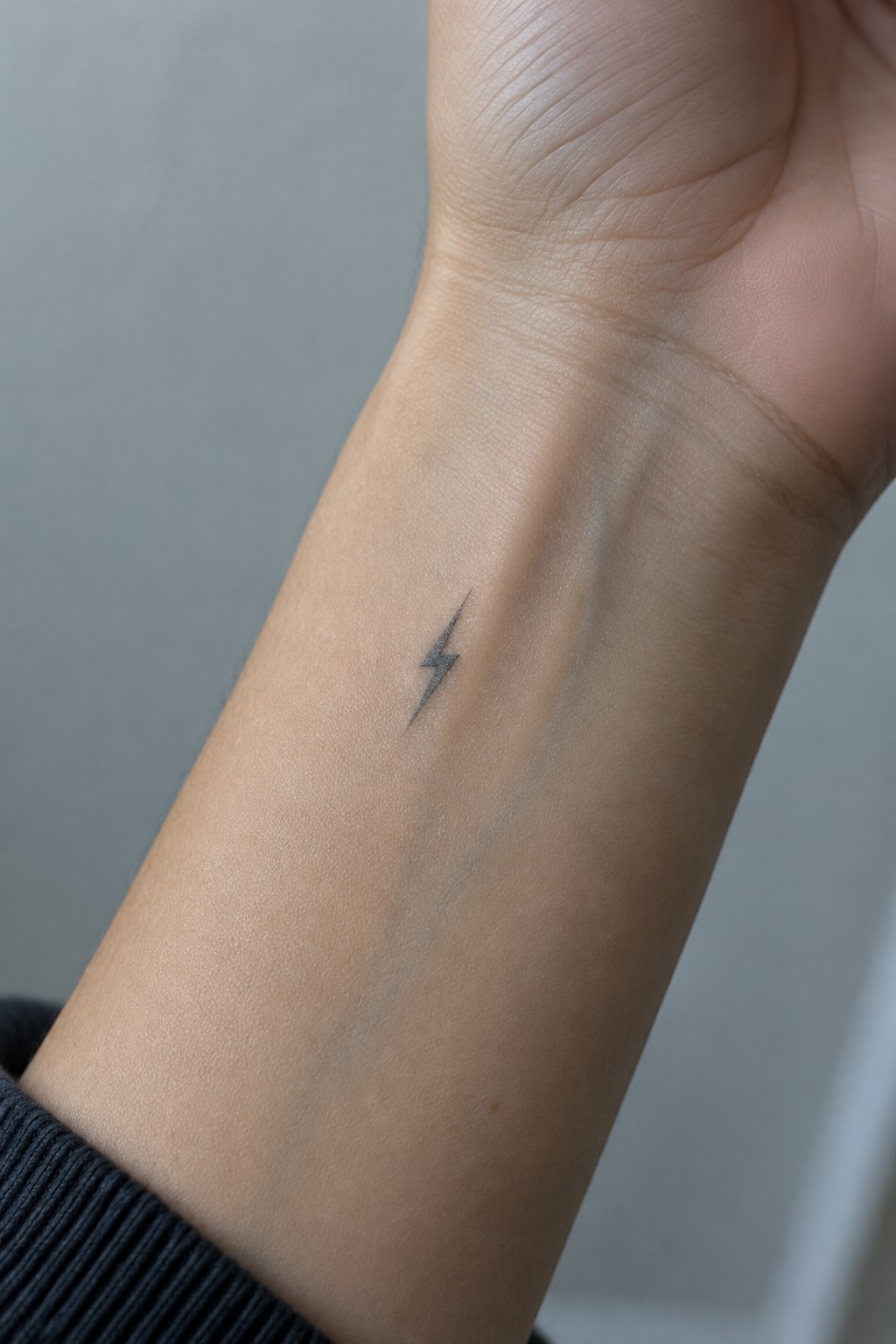 Small black lightning bolt tattoo on light-skinned inner wrist above dark sleeve