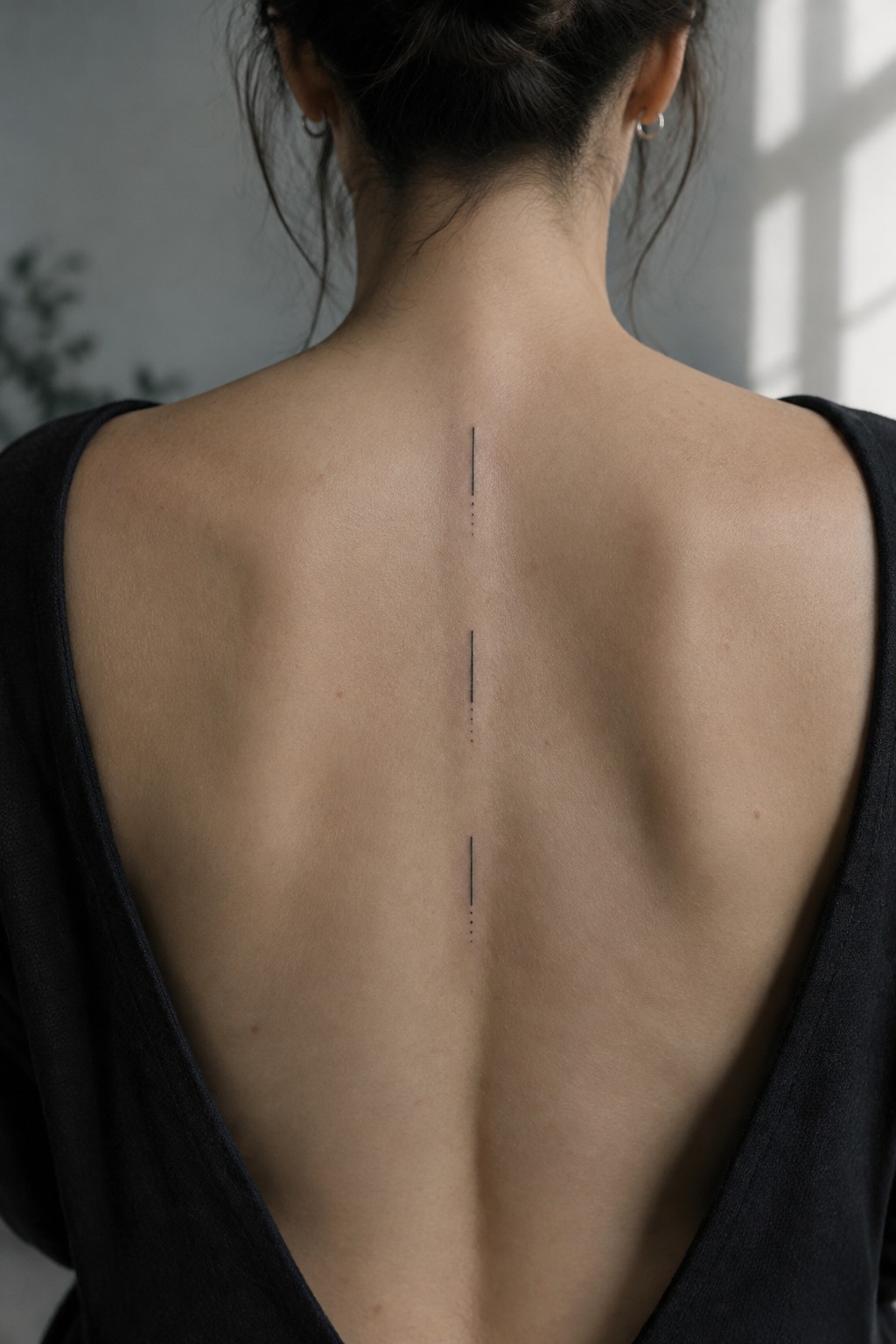 Woman's back with low black top and three vertical spine tattoos