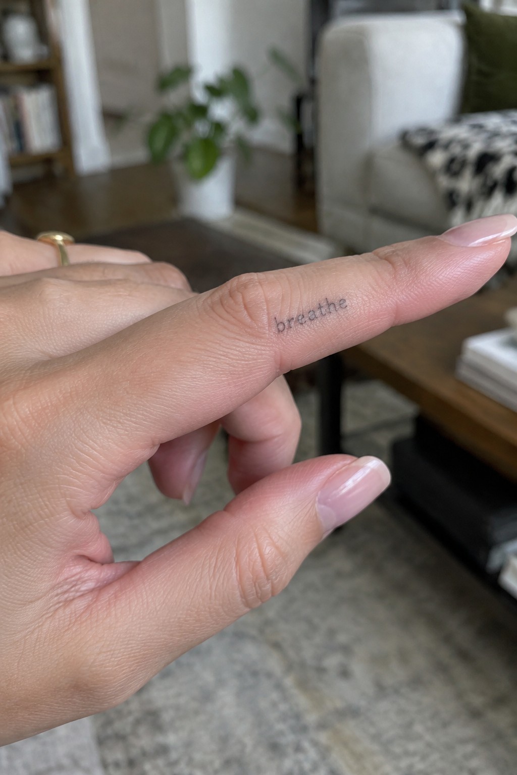 Small lowercase “breathe” tattoo in fine lettering on the side of a finger.