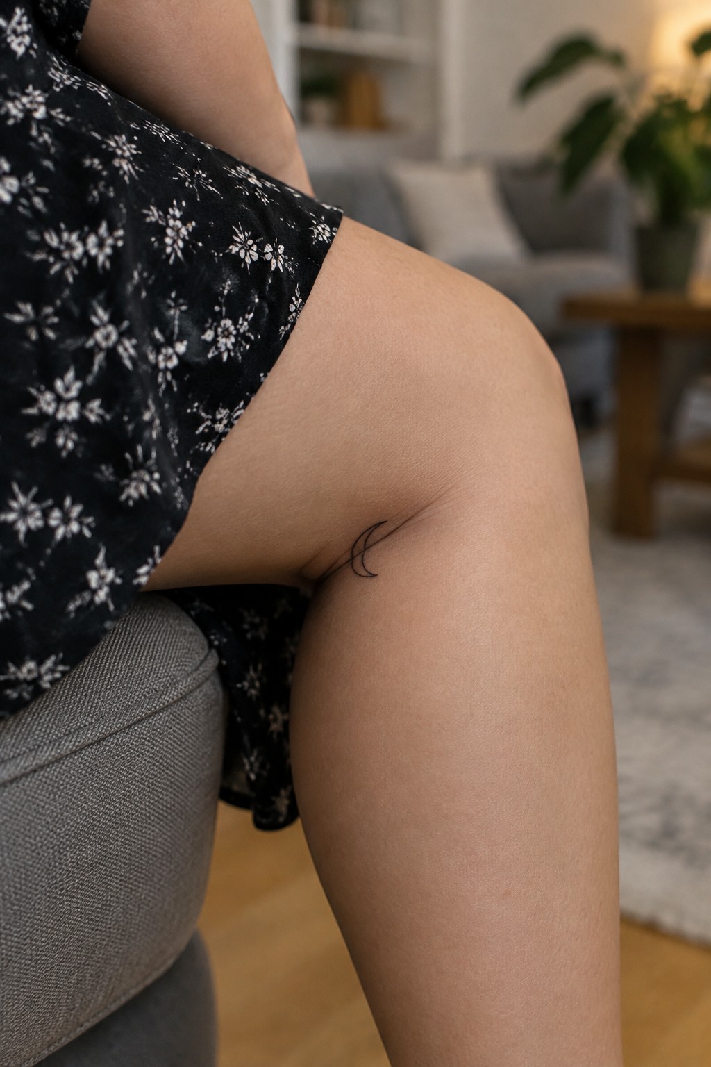 Small fine-line crescent moon tattoo on the inner thigh near the knee.