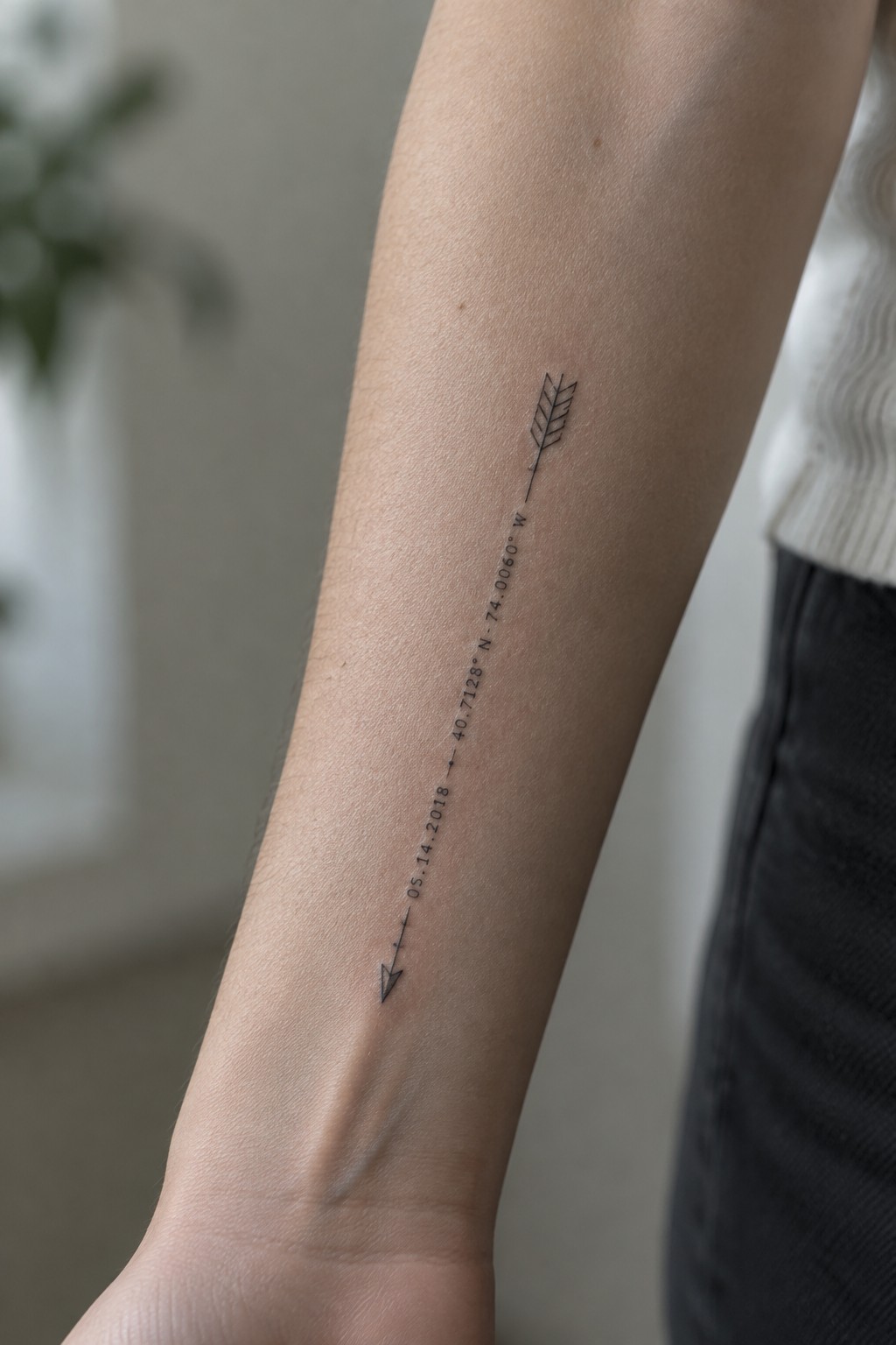 Fine-line forearm tattoo of an arrow with a feather, date, and geographic coordinates.