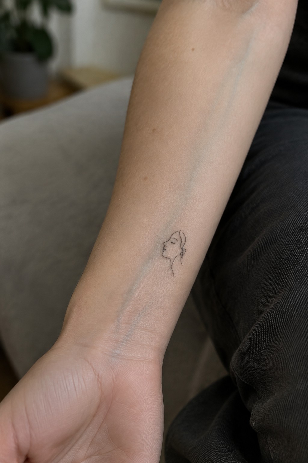 Small fine-line tattoo of a woman’s side profile on the inner forearm.