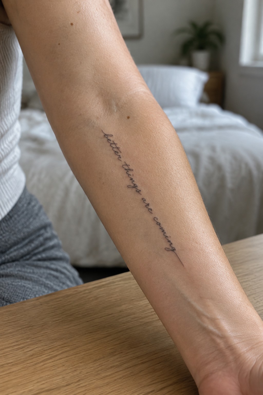 Fine-line cursive tattoo reading “better things are coming” along a woman’s inner forearm.