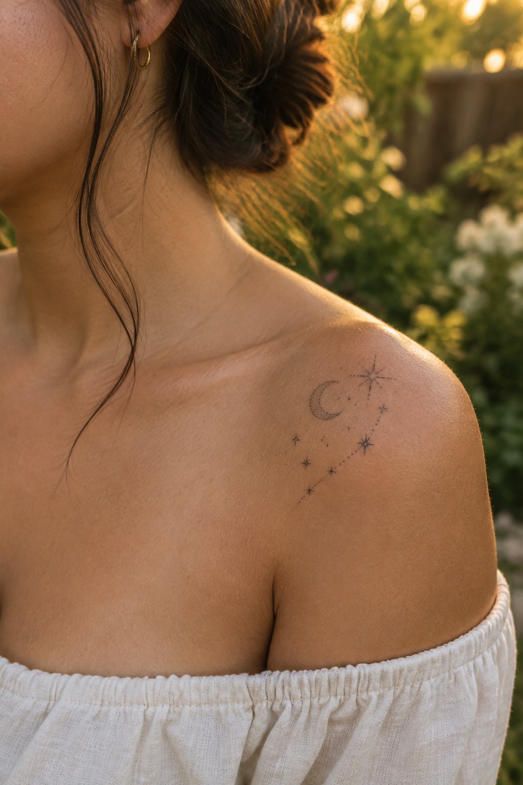 Tiny crescent moon and star constellation tattoo on a woman’s shoulder.
