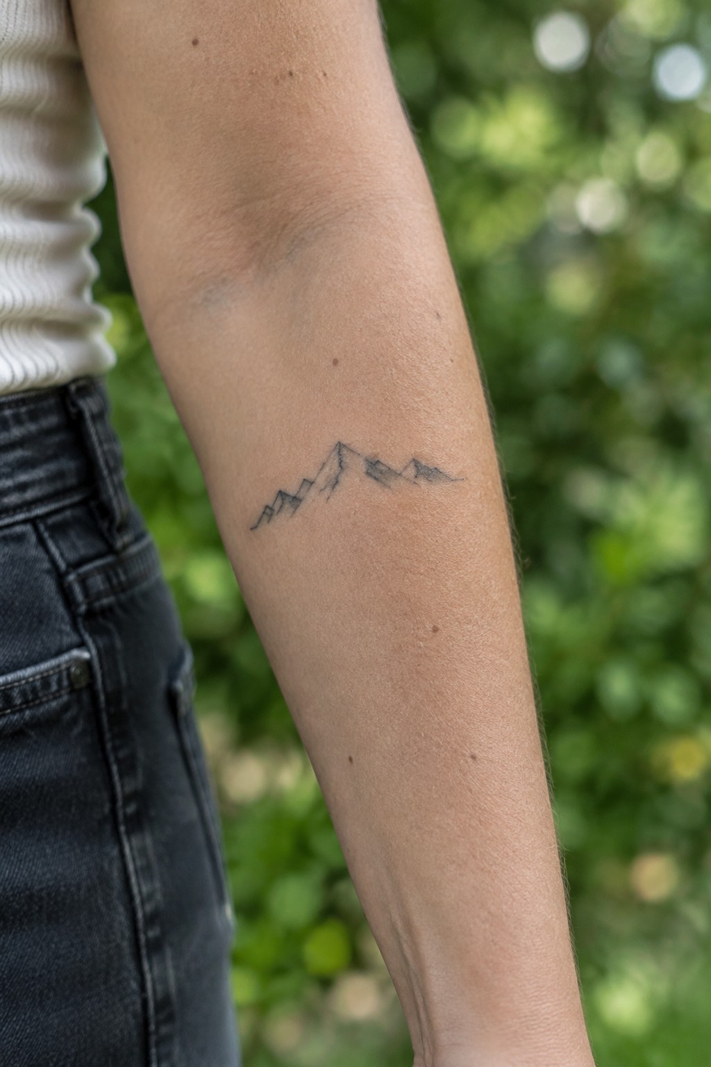 Small fine-line mountain range tattoo with light shading on the inner forearm.