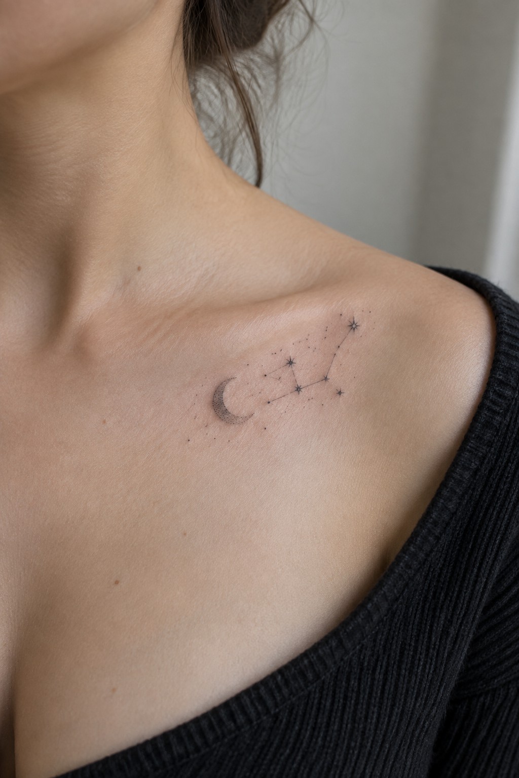 Small fine-line crescent moon and connected constellation tattoo on a woman’s collarbone.