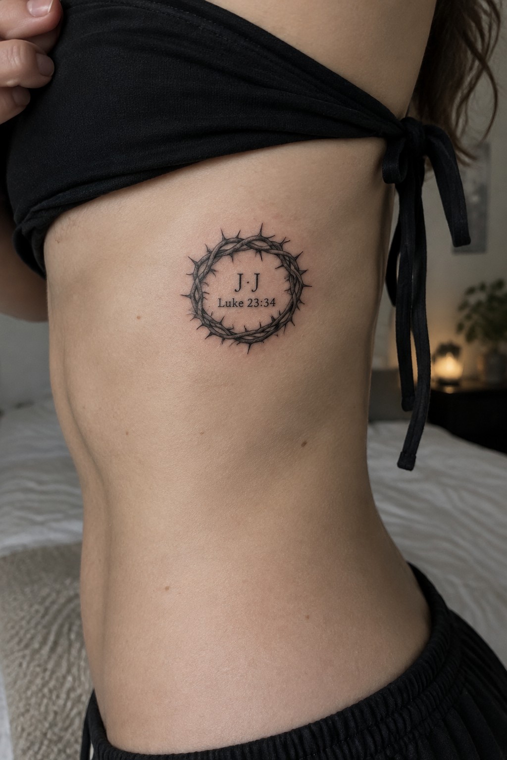 Crown of thorns tattoo with J·J and Luke 23:34 on torso under black tied top