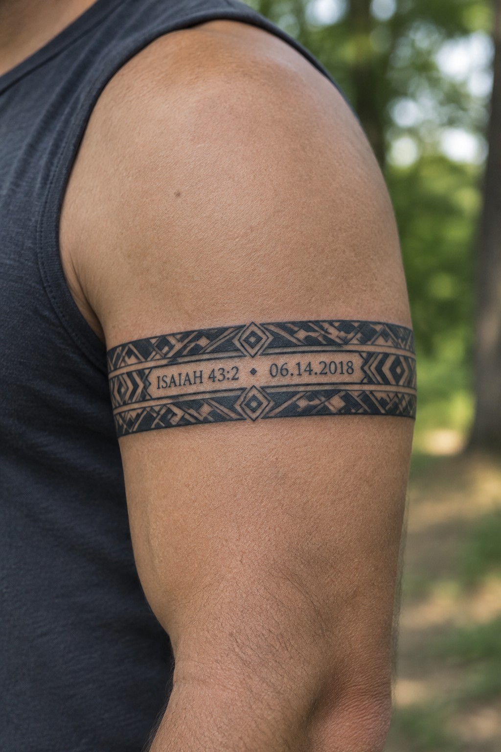 Close up of a black geometric band tattoo on a man's upper arm showing Isaiah 43:2 and the date 06.14.2018