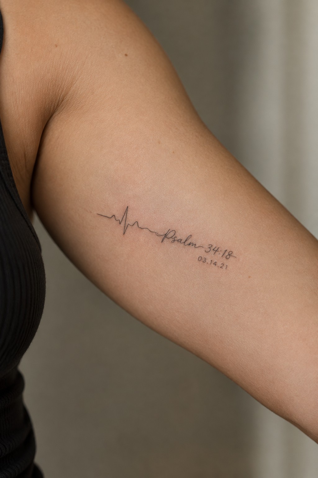 Upper arm with black heartbeat tattoo, Psalm 34:18 text, and date 03.14.21