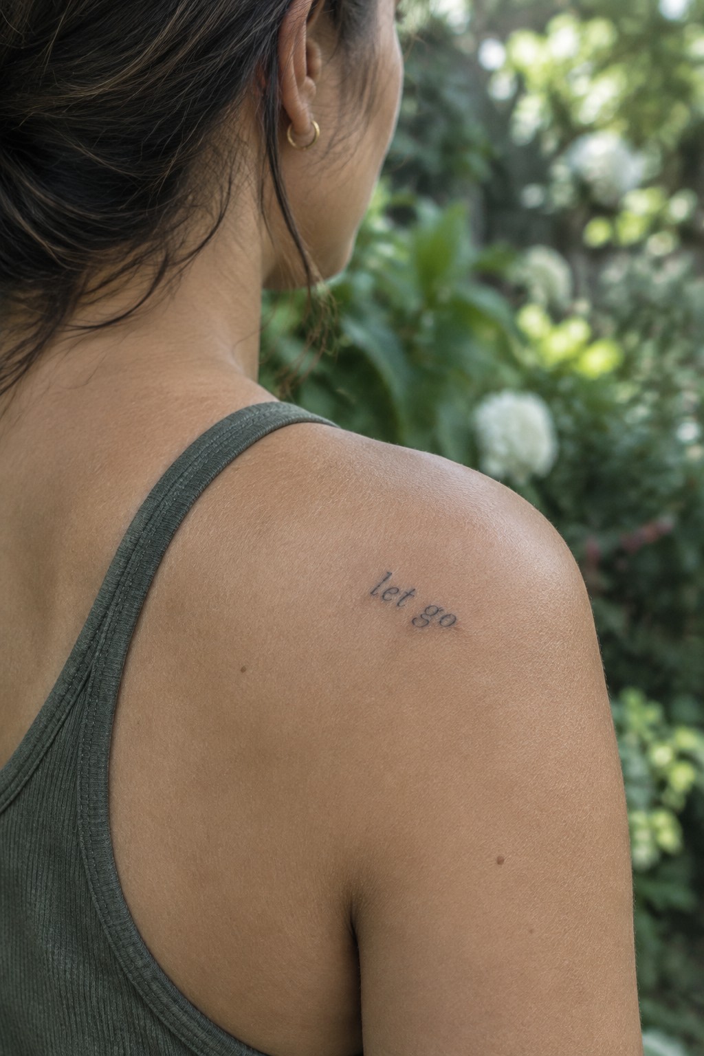 Small cursive “let go” tattoo on a woman’s upper shoulder.