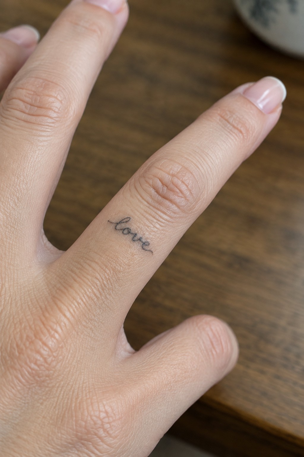 Small black cursive “love” tattoo on the side of a finger.