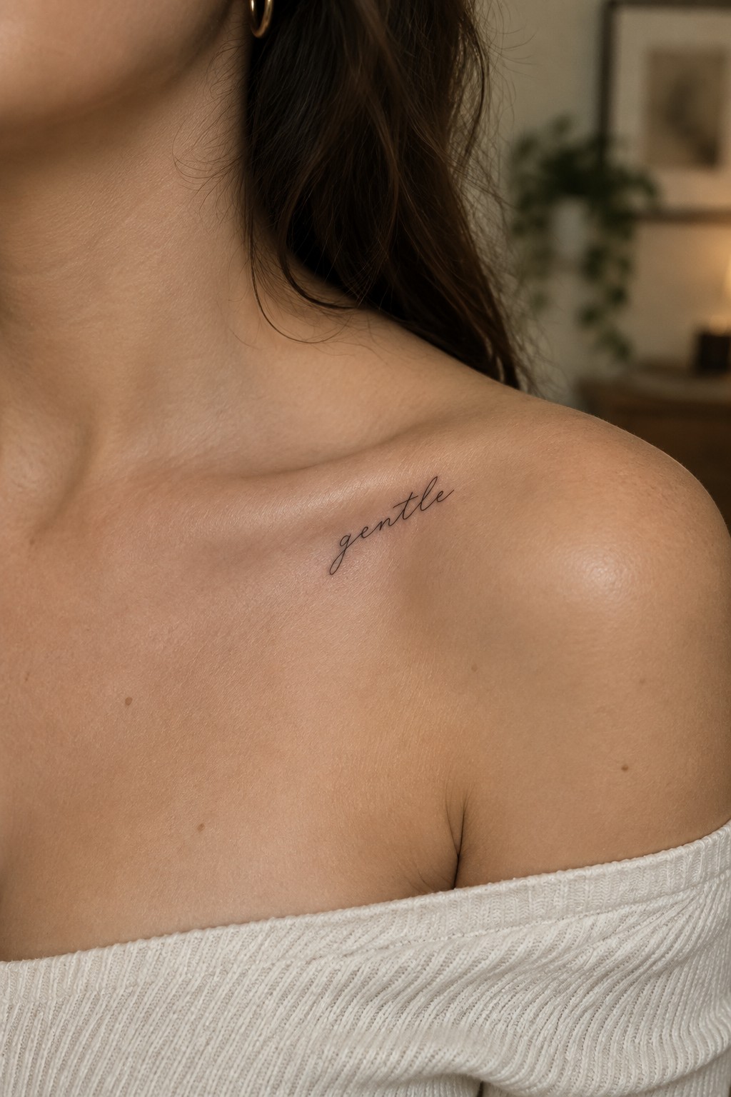 Small fine-line script tattoo reading “gentle” below the collarbone on a woman’s shoulder.