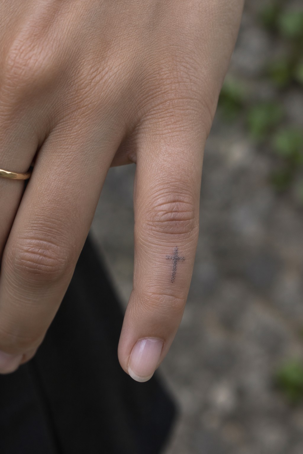 Close-up of hand with small dotted cross tattoo on finger beside gold ring.