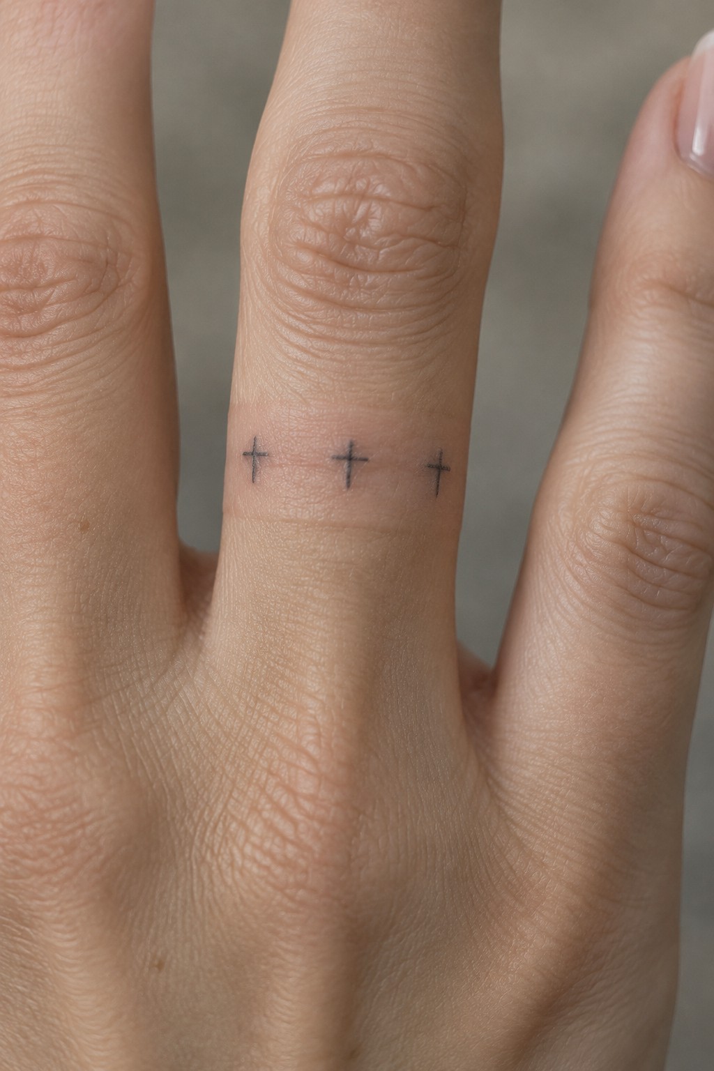 Three small black cross tattoos aligned on a light-skinned finger