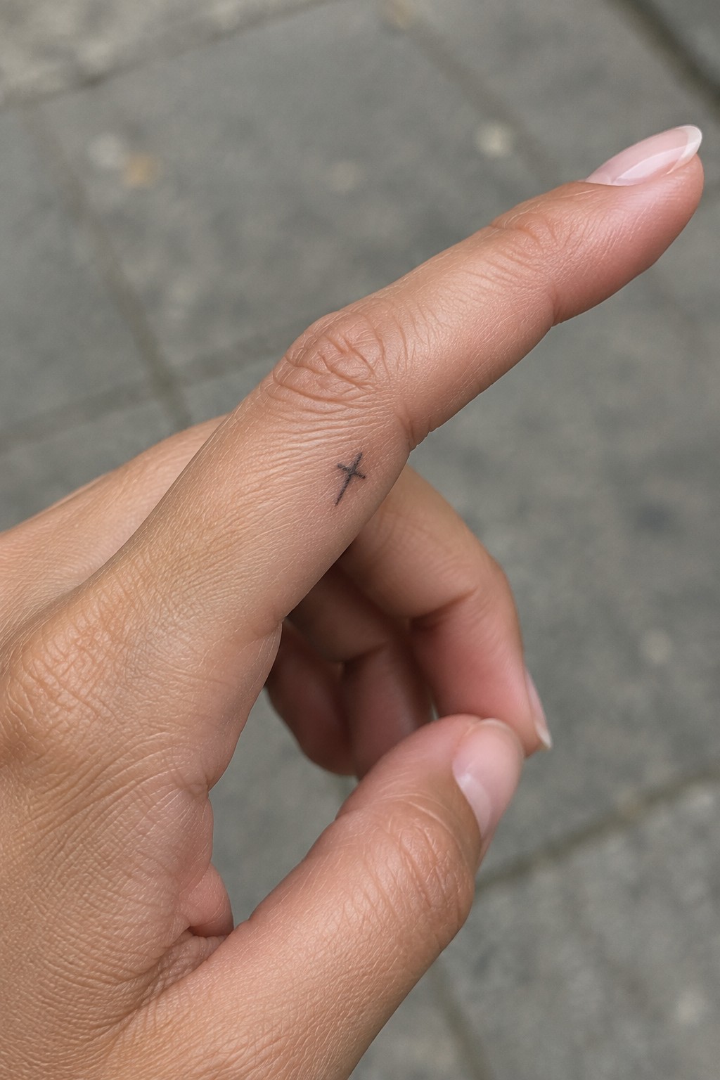 Small black cross tattoo on the side of a finger