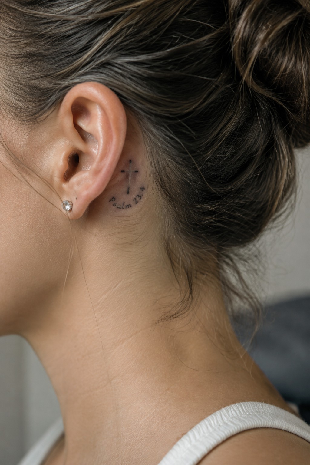 Woman's neck with cross tattoo and Psalm 23:4 text behind ear, diamond stud earring
