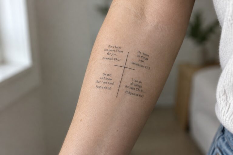 Minimalist line cross tattoo on inner forearm with four bible verses placed around the cross including Psalm 23:1 at top, Philippians 4:13 on left, Jeremiah 29:11 on right, and Psalm 46:10 at bottom