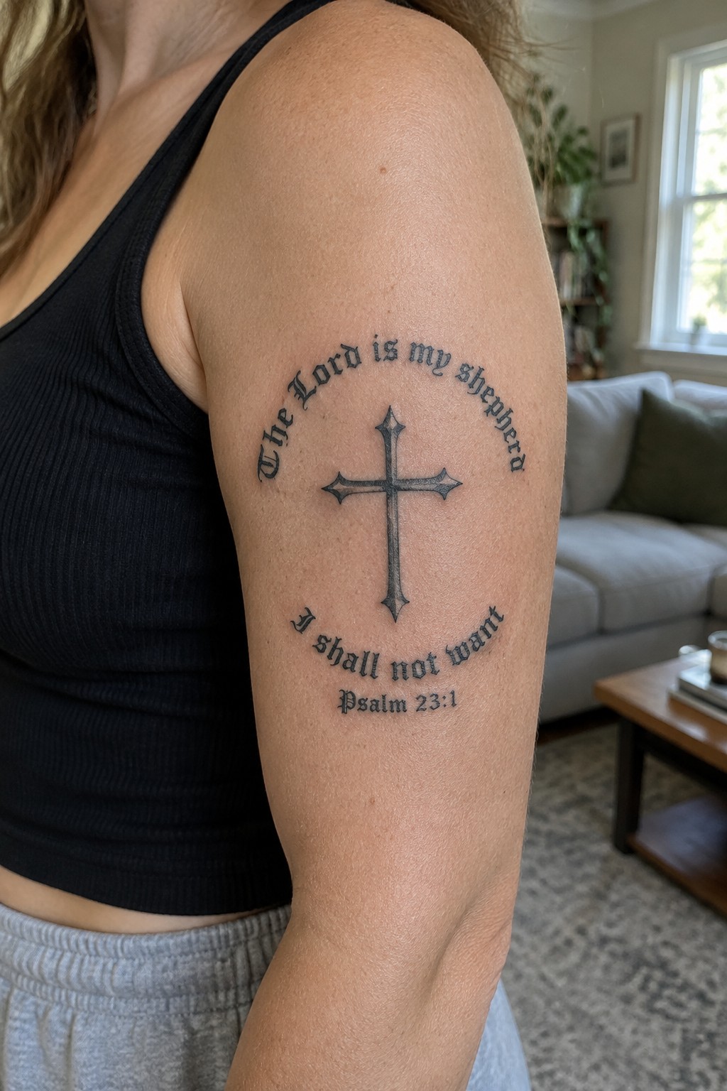 Black tank top arm with cross tattoo quoting Psalm 23:1 in living room