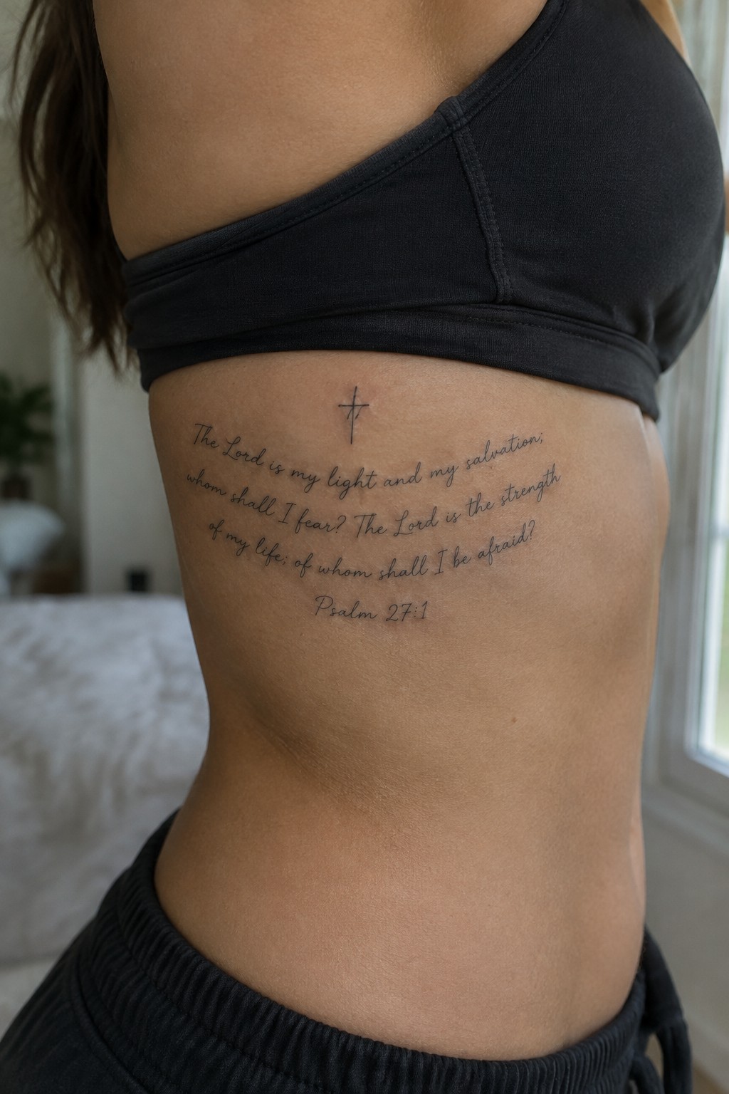 Woman's side with cross and Psalm 27:1 tattoo under black sports bra