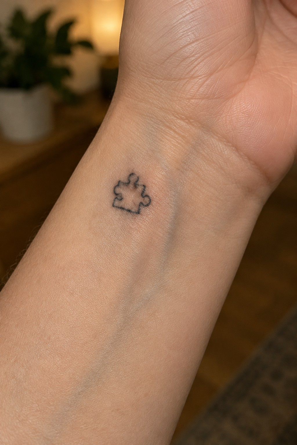 Small black outline puzzle piece tattoo on the inner wrist.