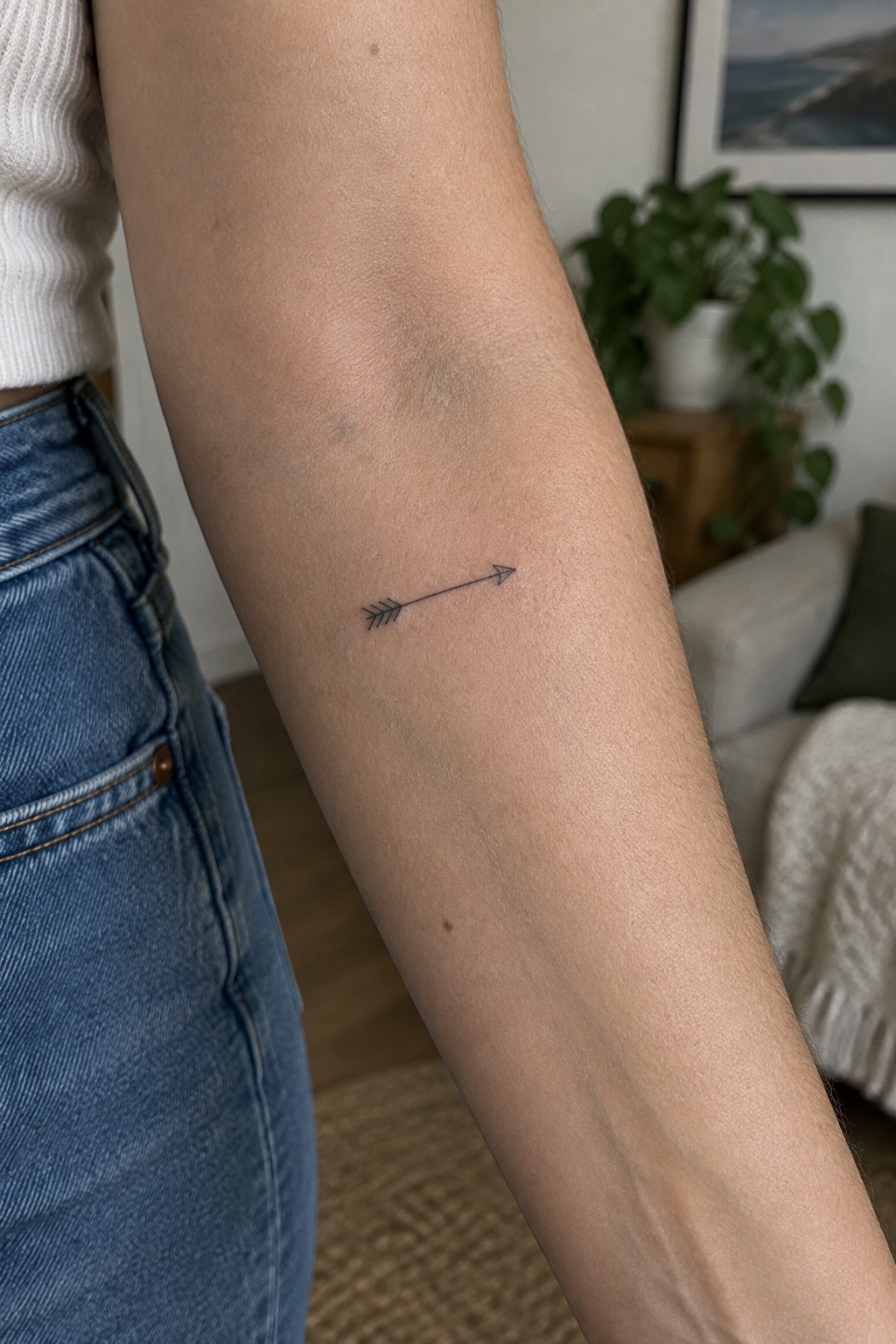 Small fine-line black arrow tattoo on the inner arm, with a pointed tip and feathered tail.