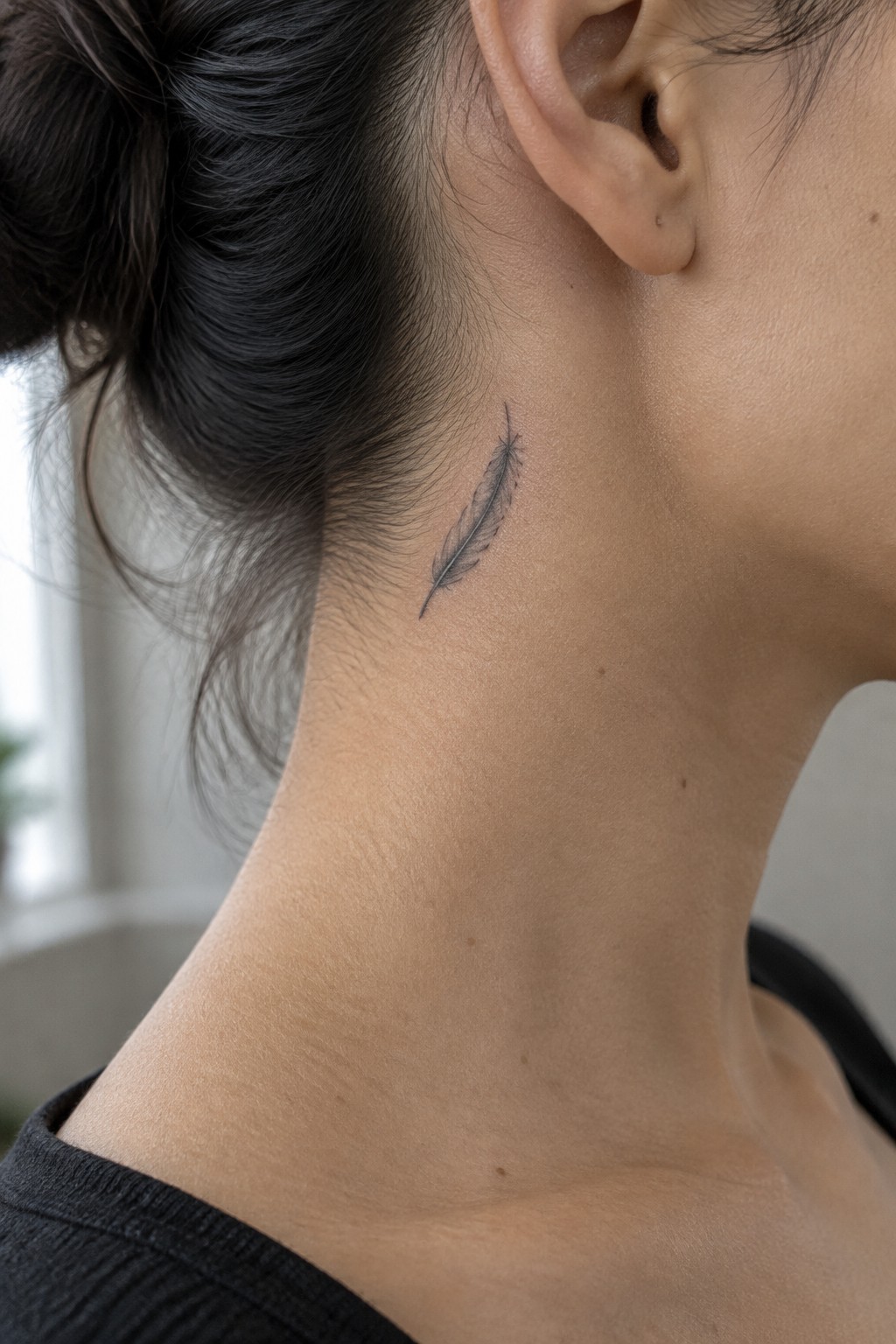 Small fine-line feather tattoo on the side of a woman’s neck below her ear.