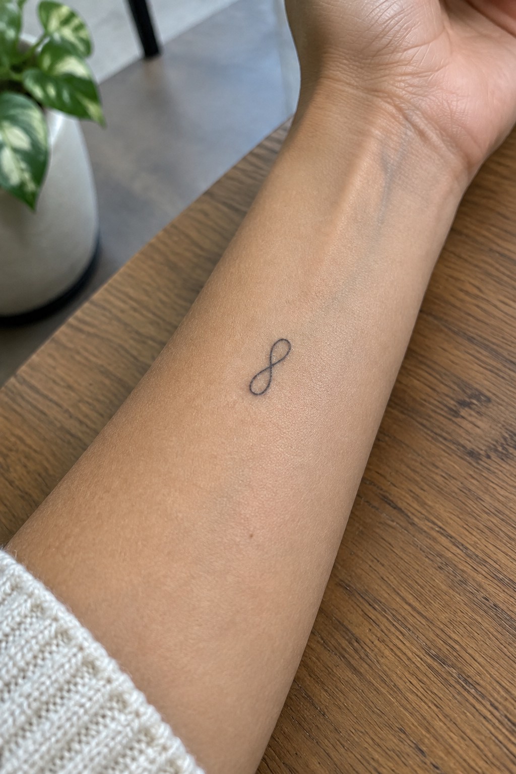 Small black infinity symbol tattoo on the inner forearm.