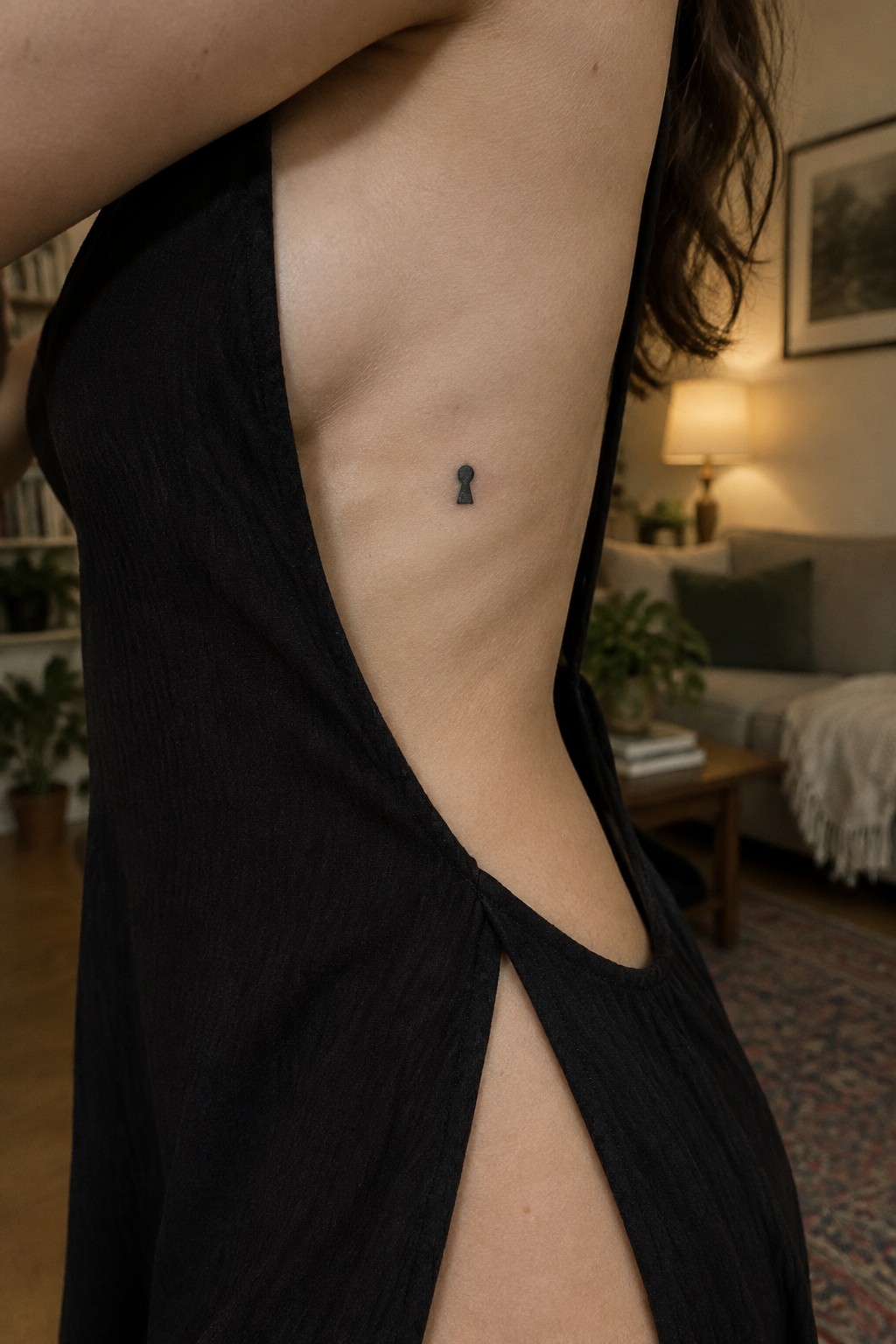Small black keyhole tattoo on the side of a woman’s ribs above a black dress.