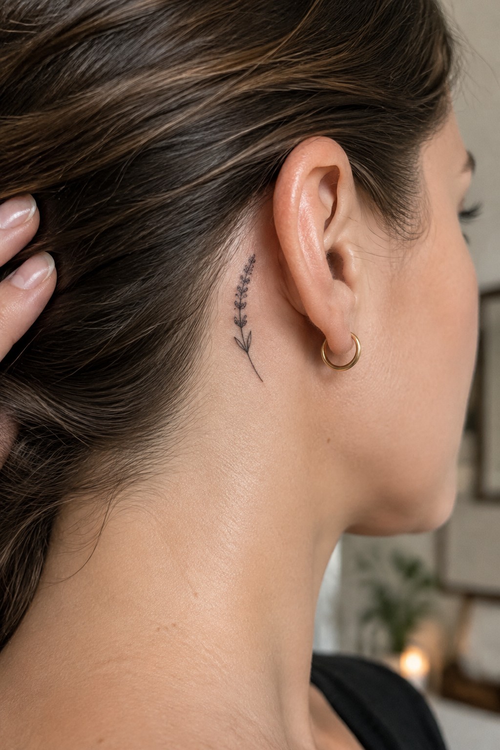 Fine line lavender sprig tattoo behind a woman's ear on the side of the neck