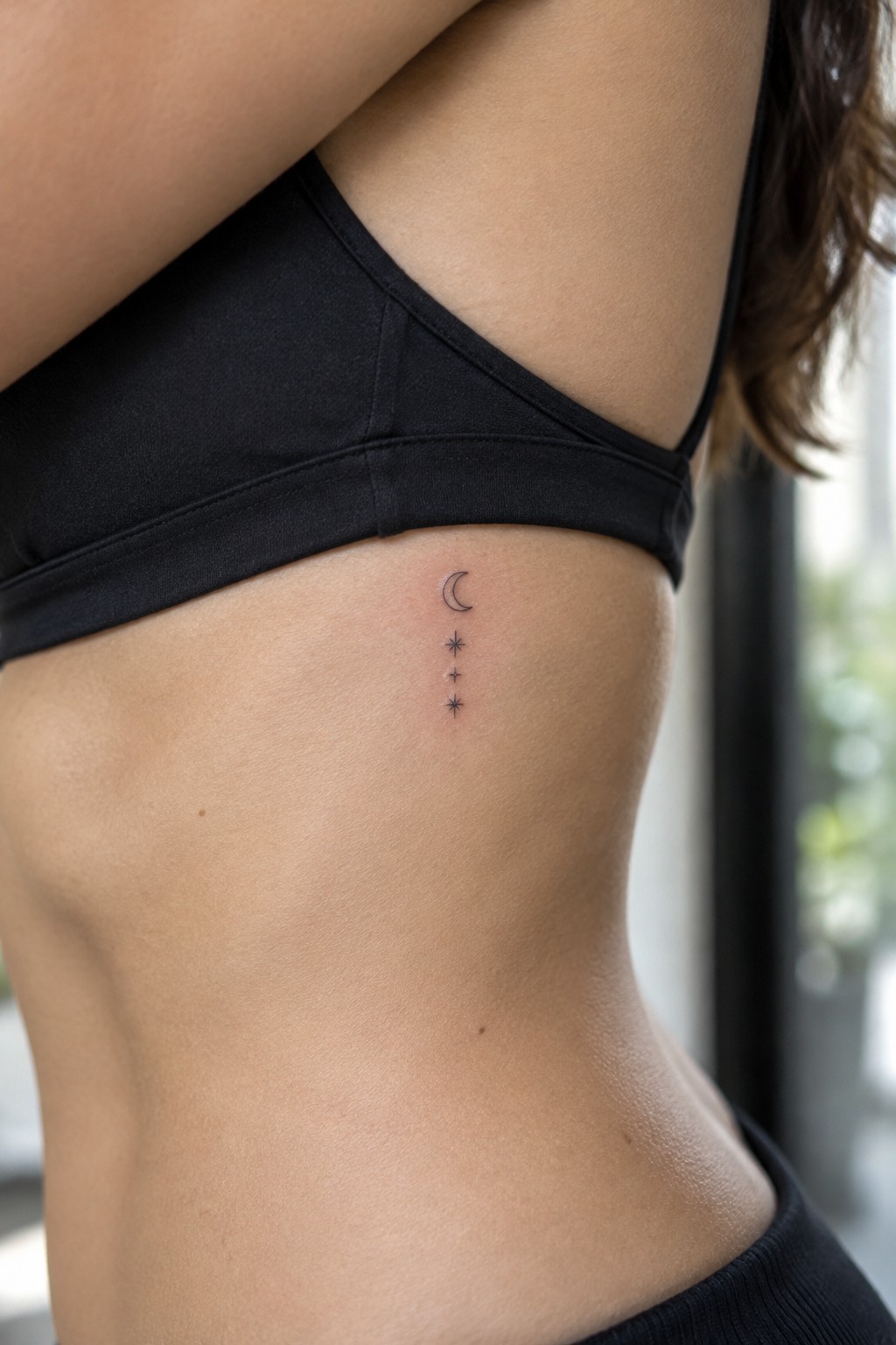 Crescent moon and stars tattoo on ribcage under black sports bra