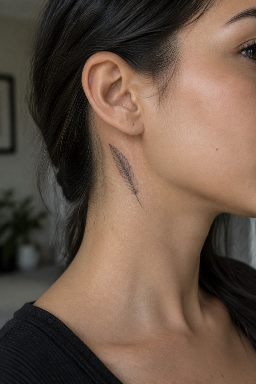 Side view of neck with small black feather tattoo below ear, dark hair pulled back