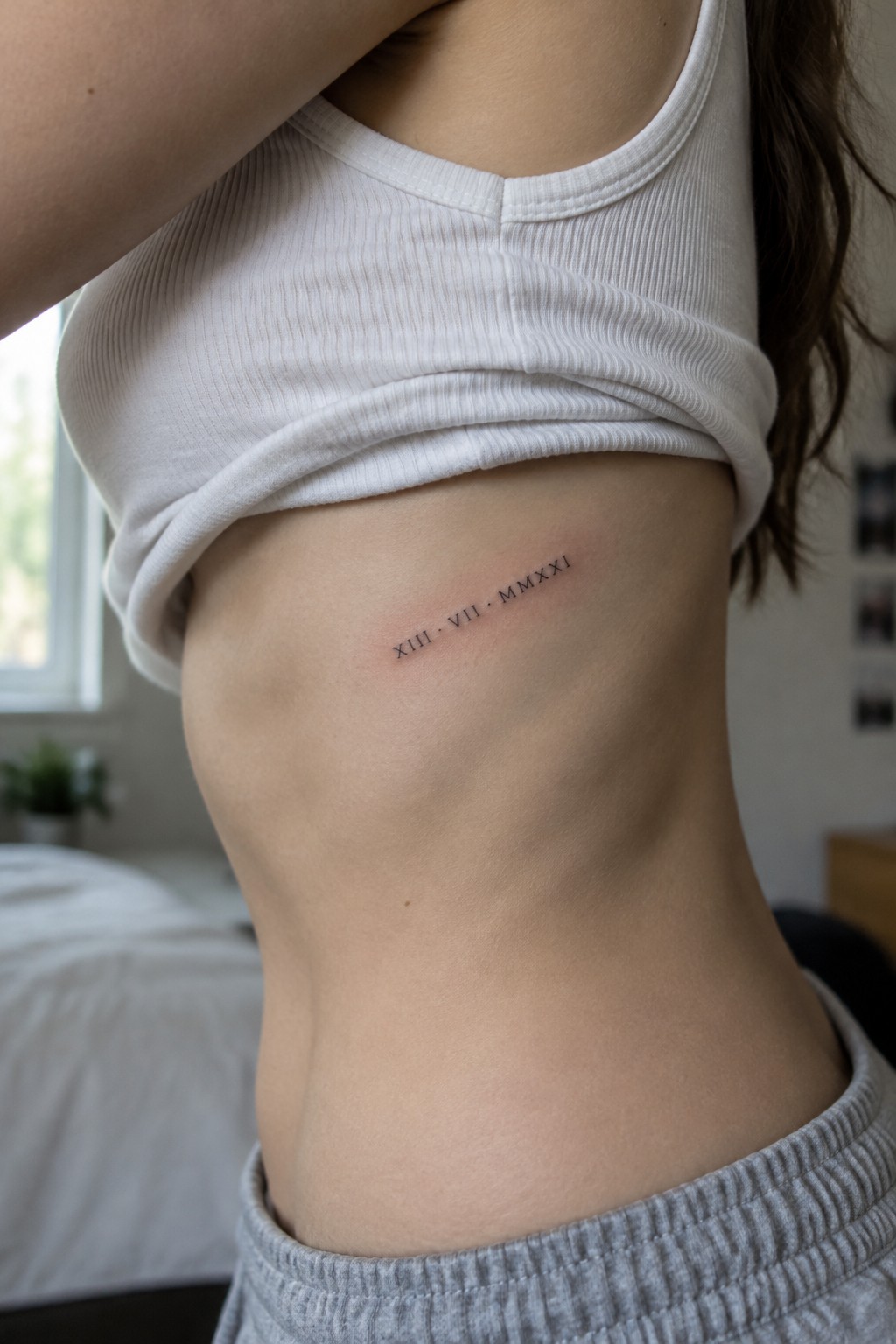 Lifted white tank top reveals Roman numeral tattoo on side torso above gray sweatpants