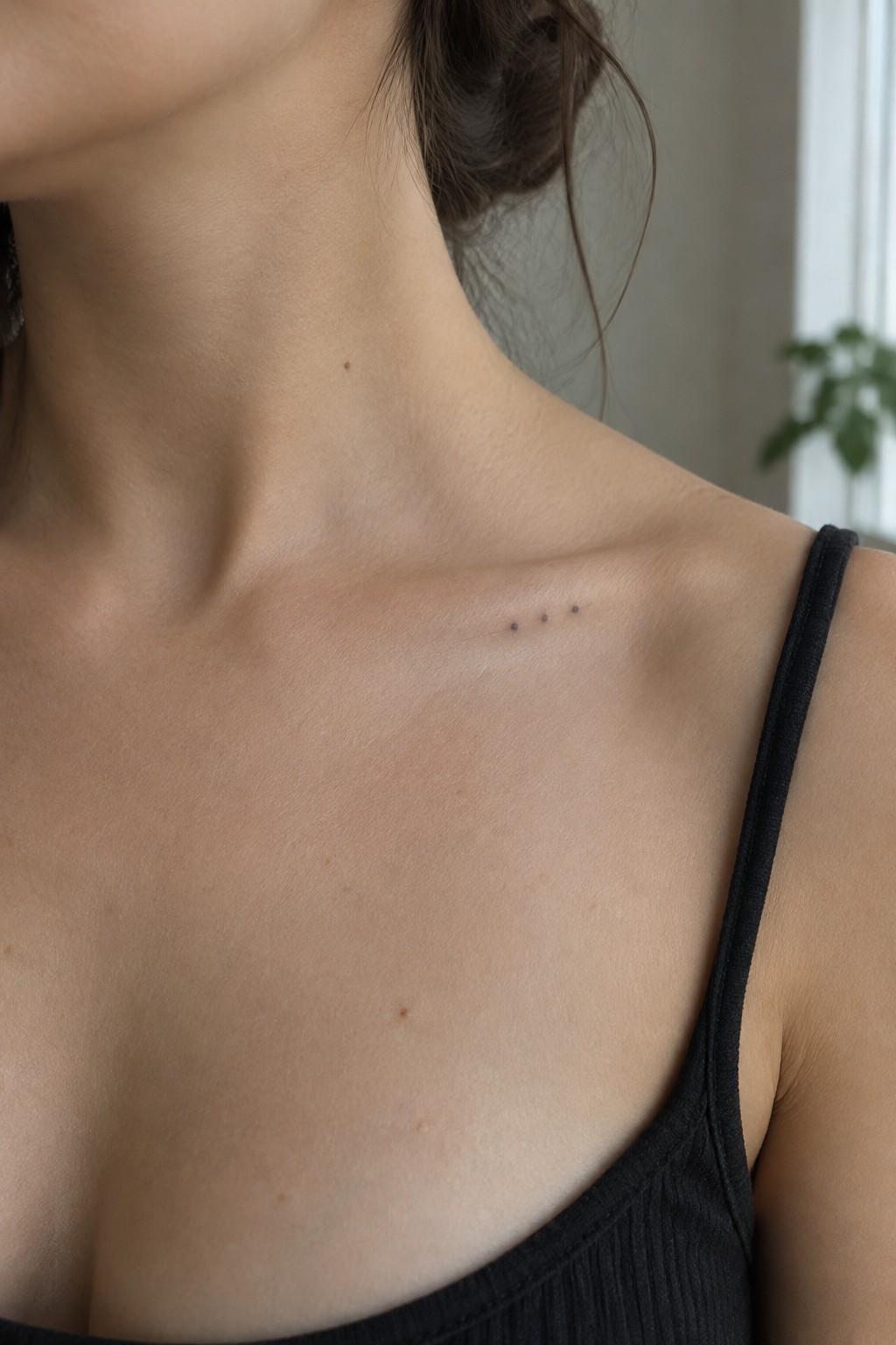 Three small dot tattoos on collarbone above black tank top strap