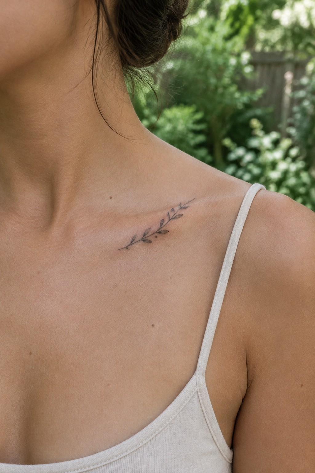 Small fine line tattoo of a leafy stem placed horizontally on the collarbone area.