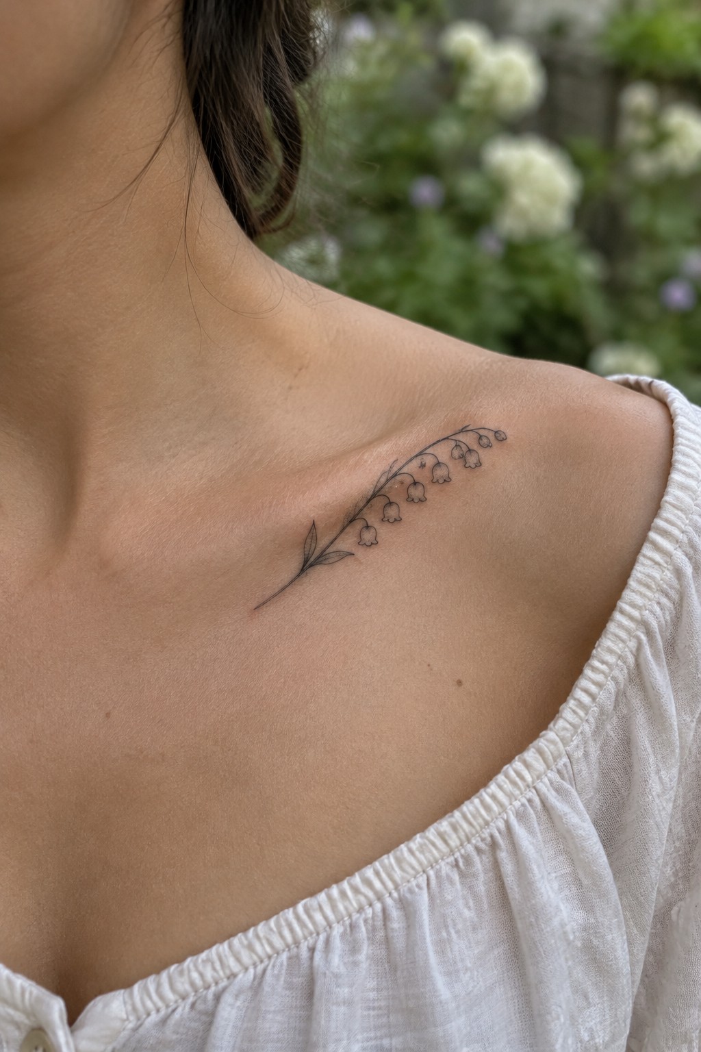 Delicate black lily of the valley tattoo on shoulder above white off-shoulder top