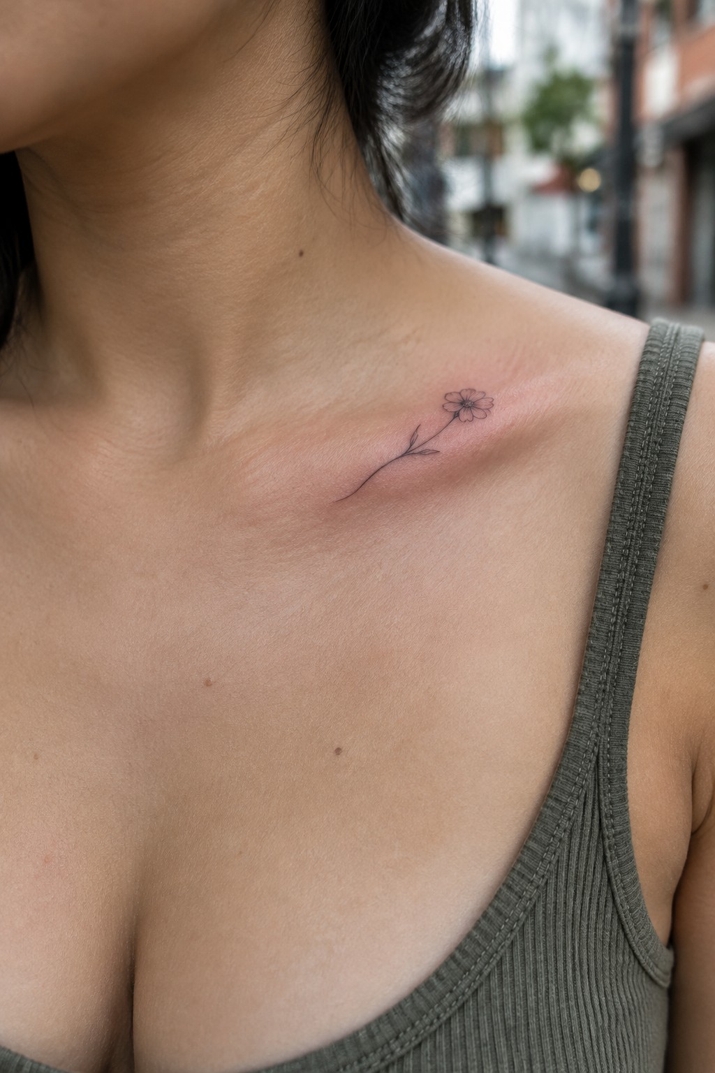 Small flower tattoo on collarbone above olive green ribbed tank top