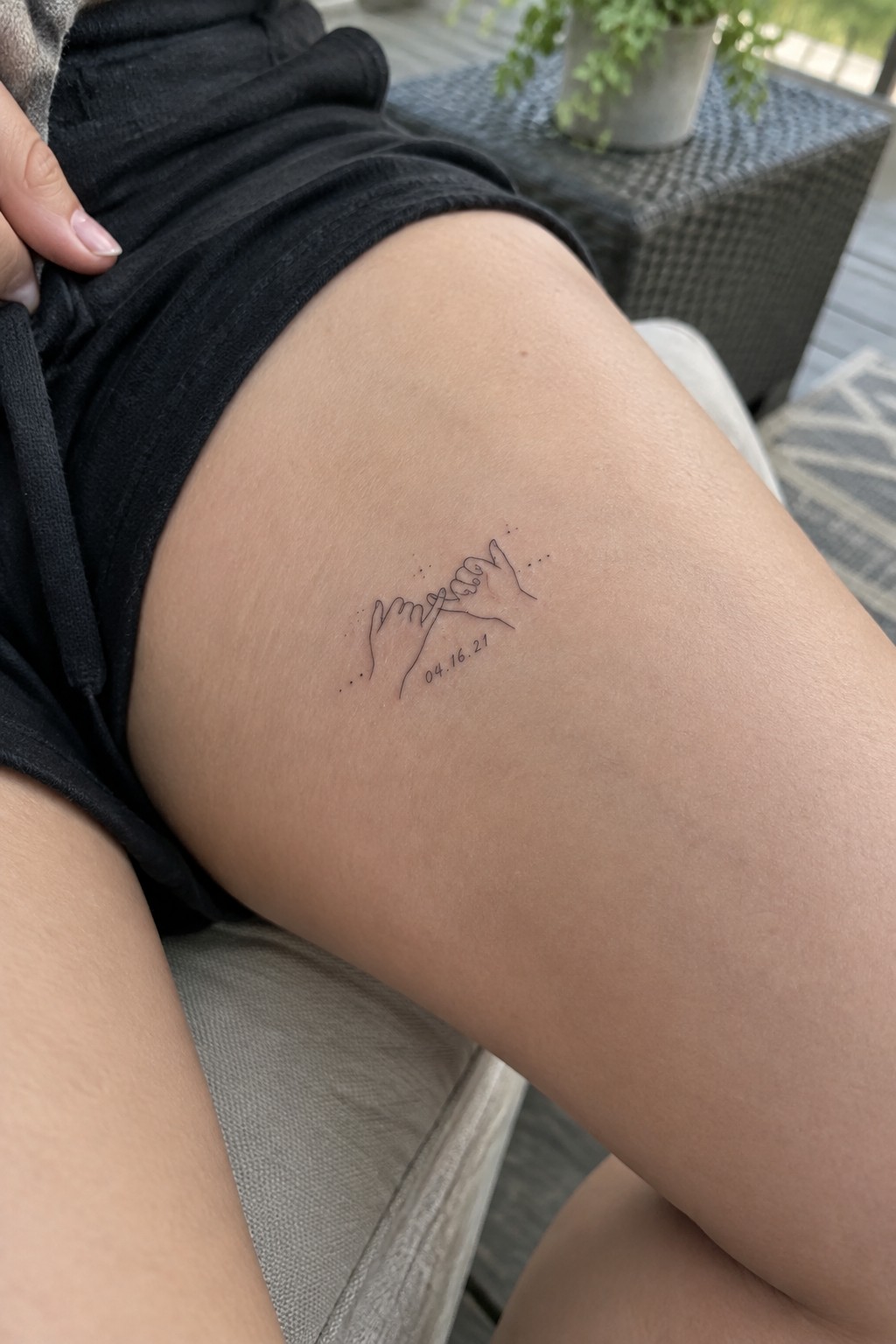 Black shorts and thigh with line-art pinky promise tattoo and date 04.16.21
