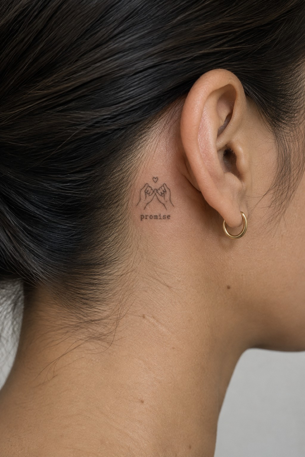 Fine line tattoo behind the ear showing two hands doing a pinky promise with a small heart above and the word promise underneath.