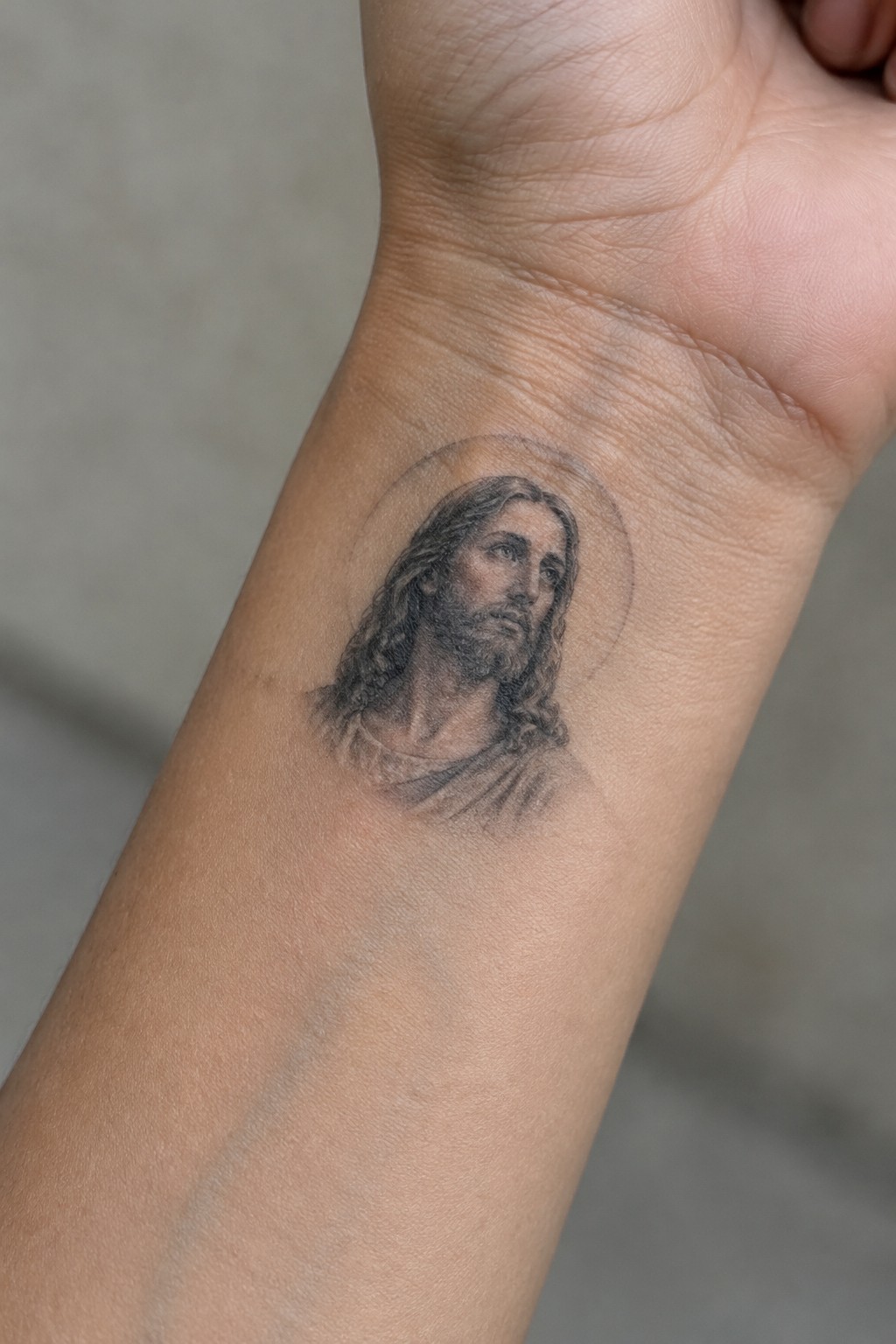 Small realistic black and gray tattoo of Jesus with a halo on the inner wrist