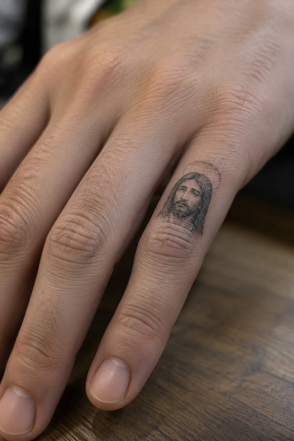 Black and gray tattoo of Jesus with halo on ring finger of hand