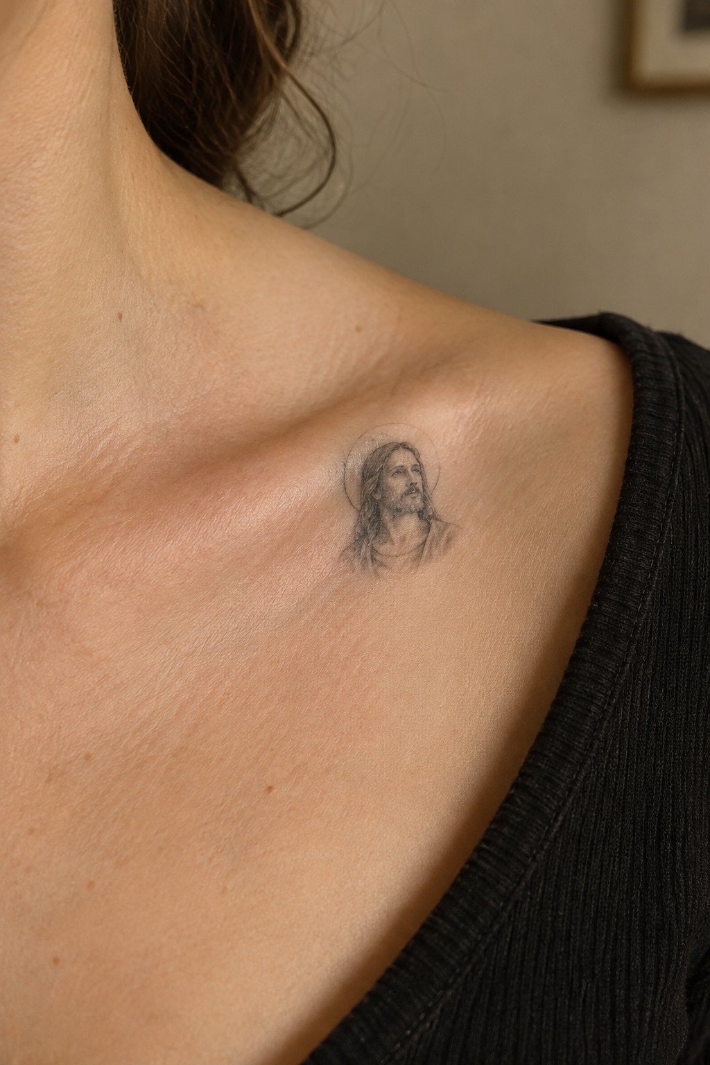 Small black and gray Jesus portrait with halo tattooed on the upper shoulder near the collarbone