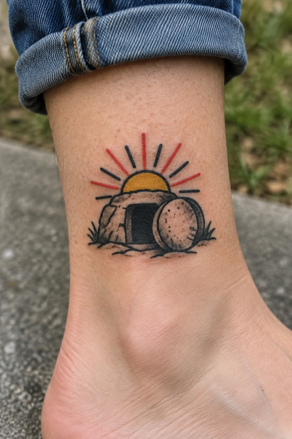 Tattoo of an empty stone tomb with a rolled boulder and rising sun on the ankle