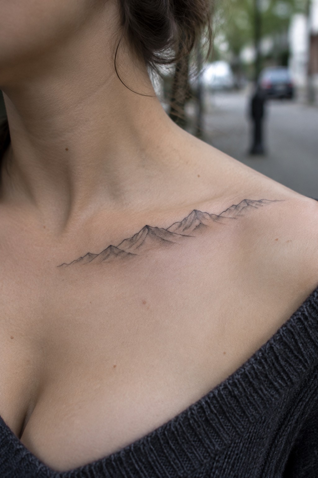 Fine-line mountain range tattoo stretching across a woman’s collarbone.