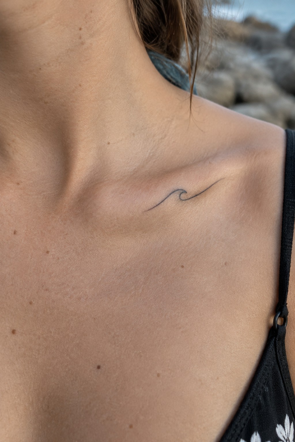 Small fine-line wave tattoo along a woman’s collarbone.