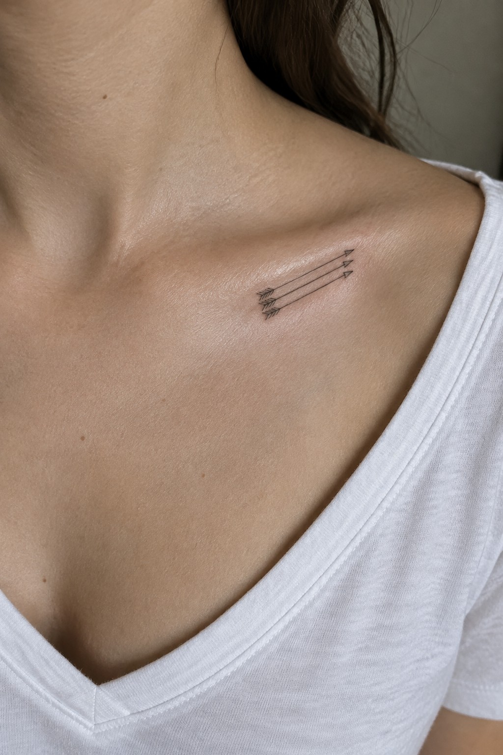Three small fine-line arrows tattooed below the collarbone and pointing toward the shoulder.