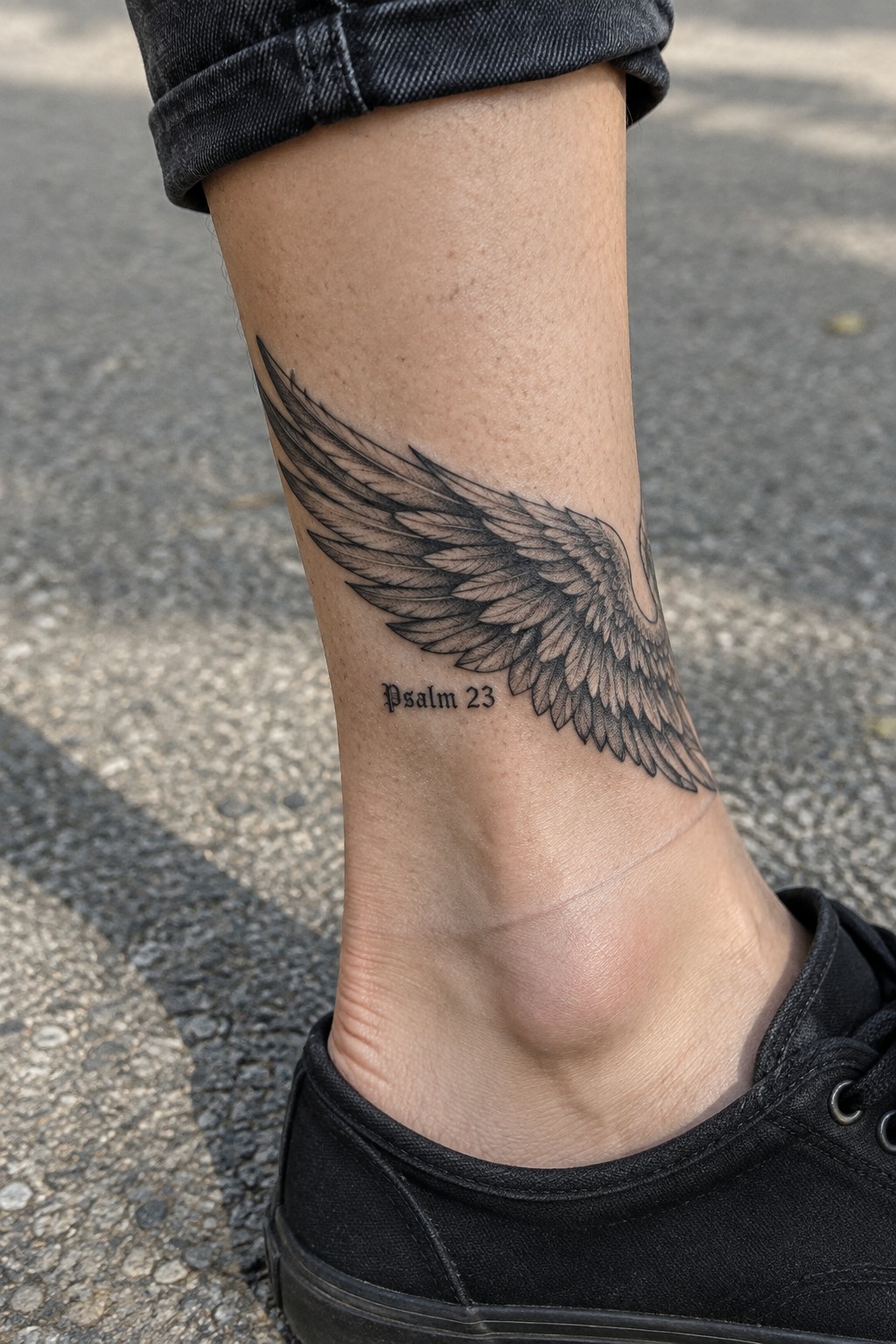 Psalm 23 wing tattoo on ankle with cuffed jeans and black sneaker