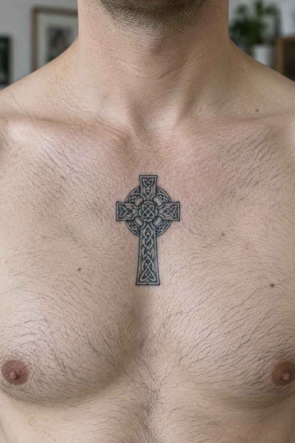 Man's hairy chest with intricate black Celtic cross tattoo centered.