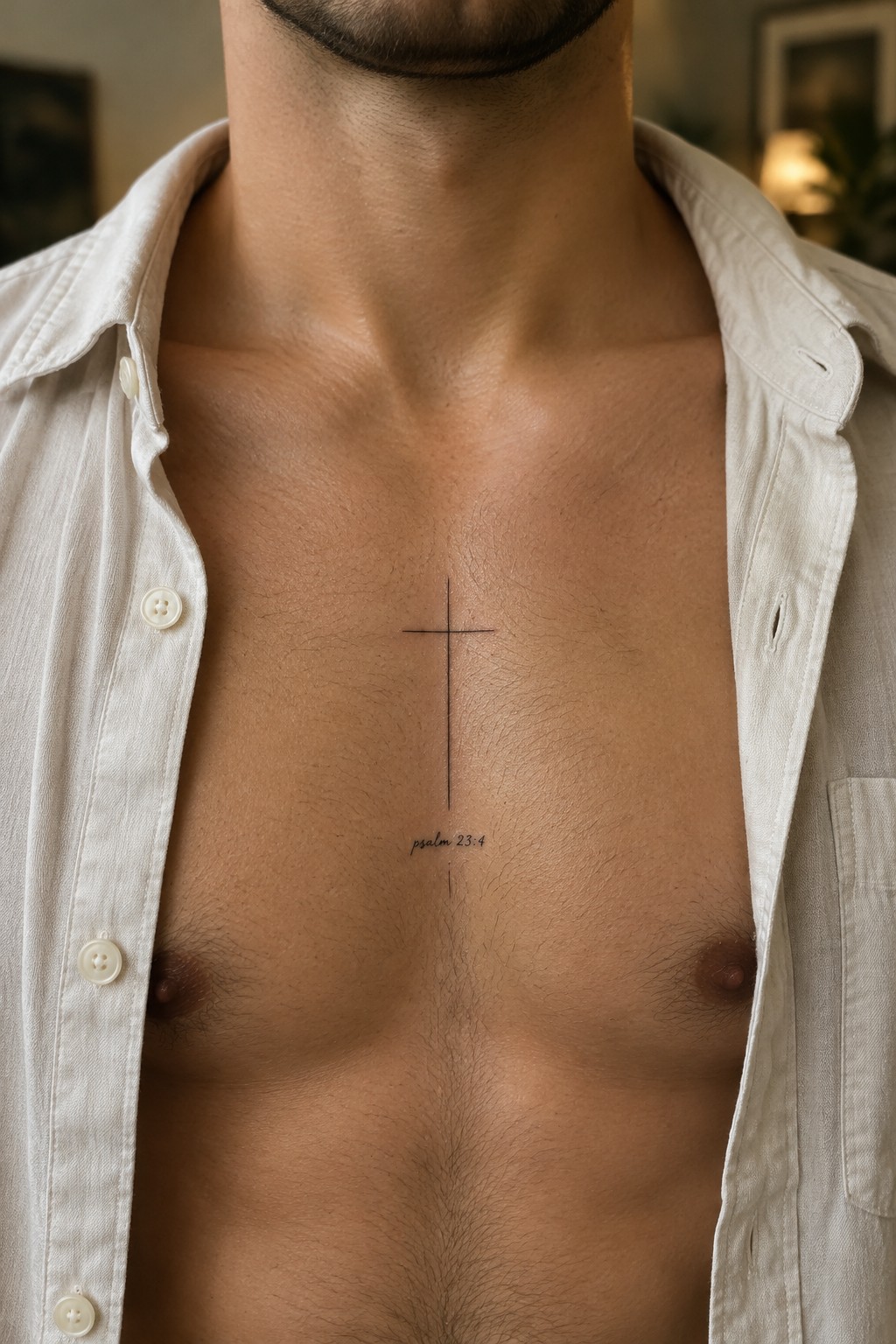 Small black cross tattoo with psalm 23:4 text below it on a man's bare chest, centered on the sternum.